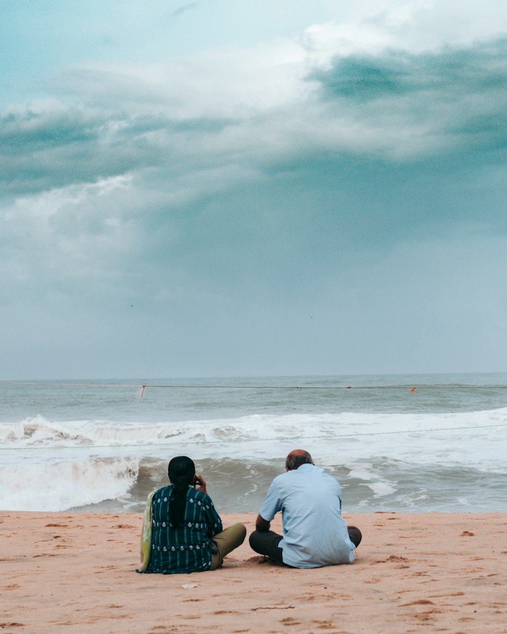 a man and woman sitting on a beach looking at the ocean