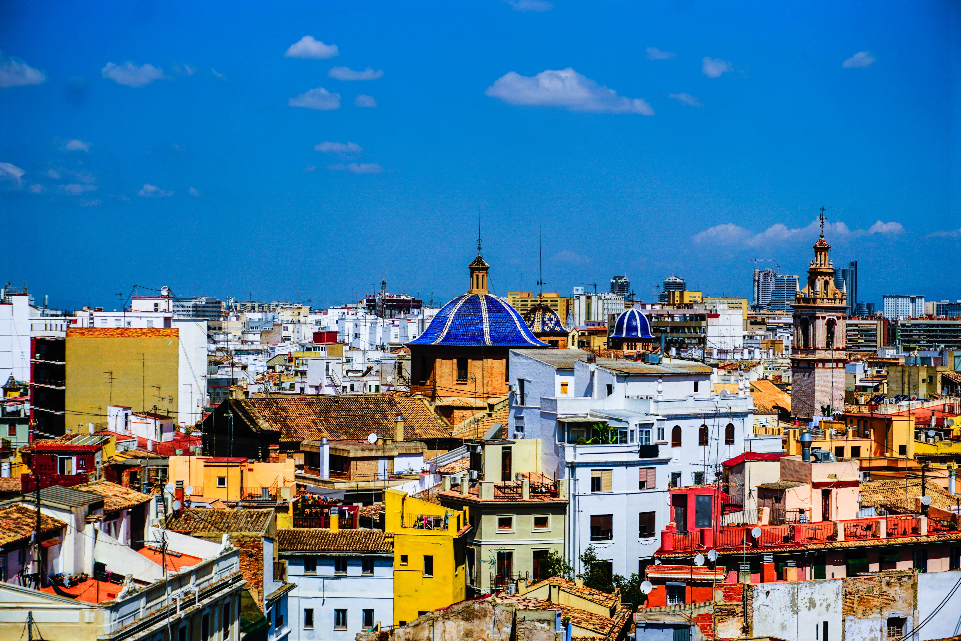 Terracotta rooftops across Valencia's old town, with a blue-tiled church dome and bell towers under a bright sky