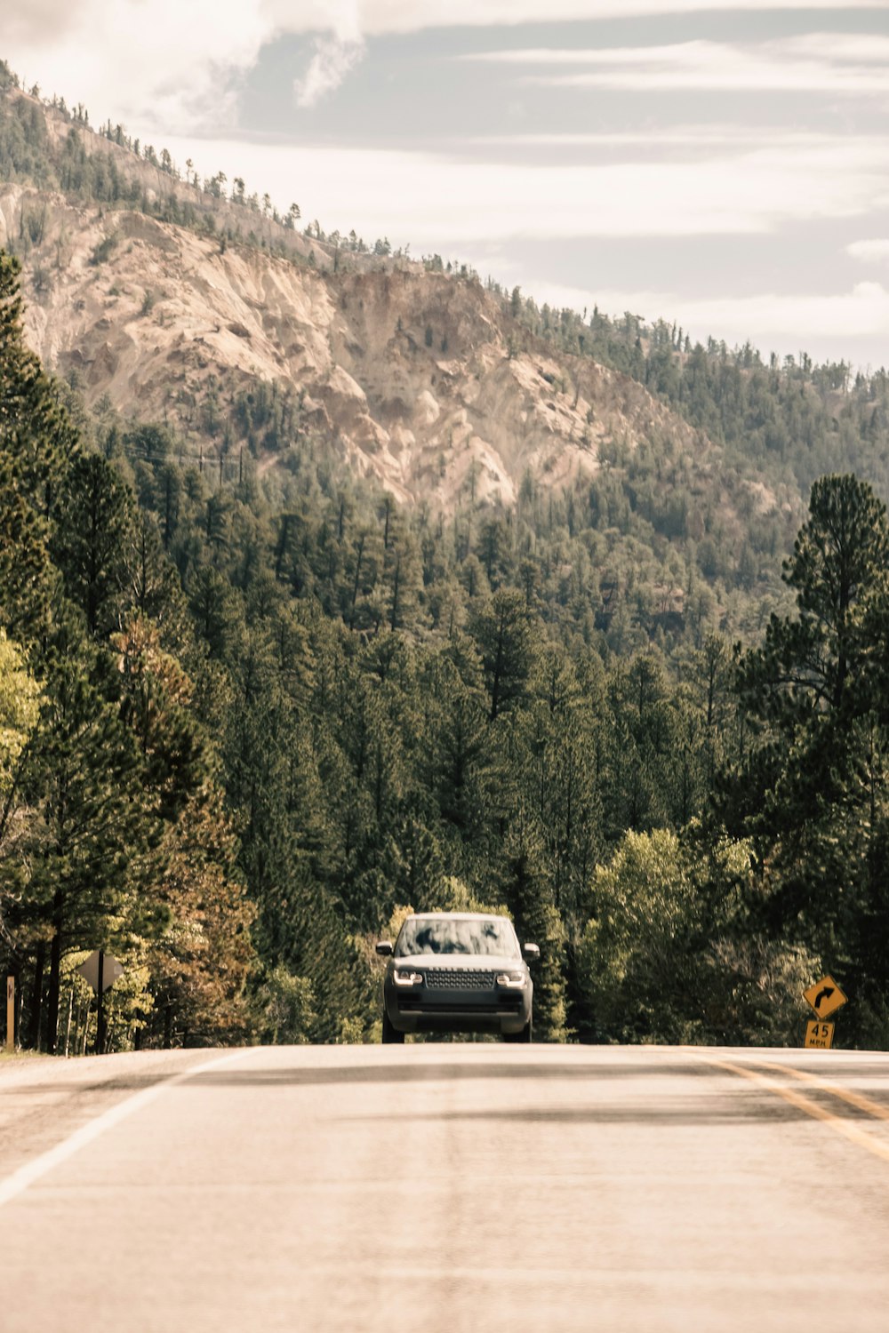 a car driving on a road with trees and mountains in the background