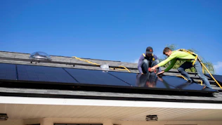 A technician installing solar panels on a sunny residential rooftop with clear blue skies.