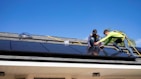 A technician installing solar panels on a rooftop on a sunny day