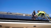 A team of professionals installing a roof on a residential building under a clear blue sky.