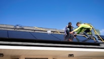 Technicians installing solar panels on a rooftop under clear blue skies.