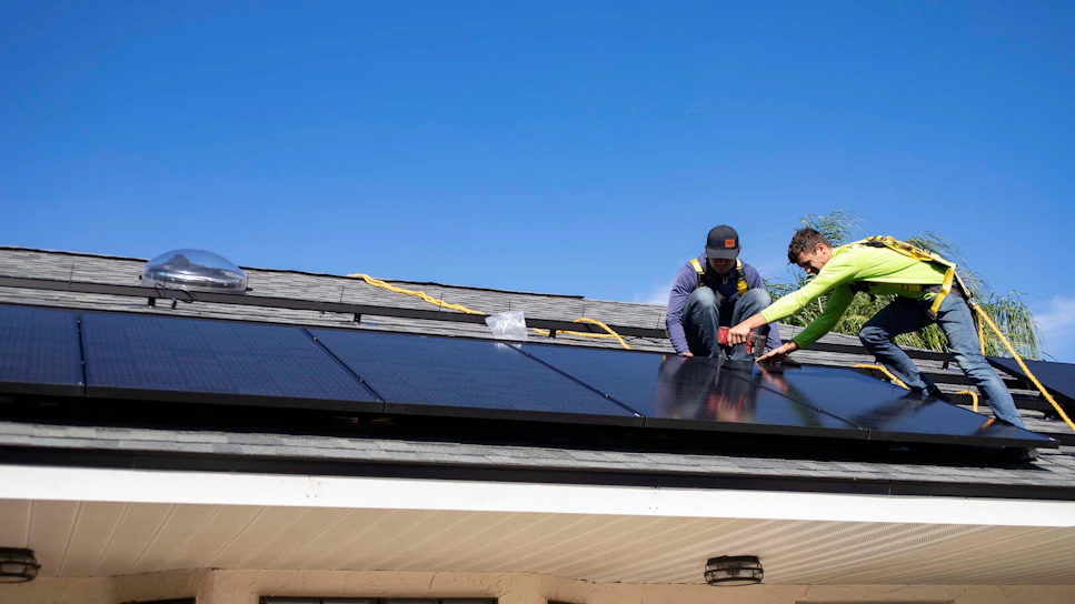 A friendly BGK Handy Services team member repairing a roof under a bright blue sky.
