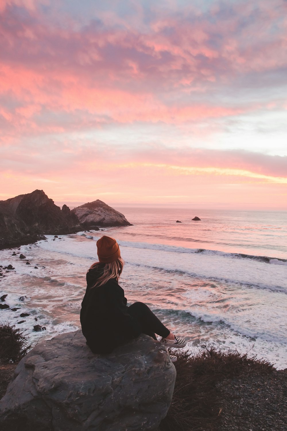 a person sitting on a rock looking at the ocean