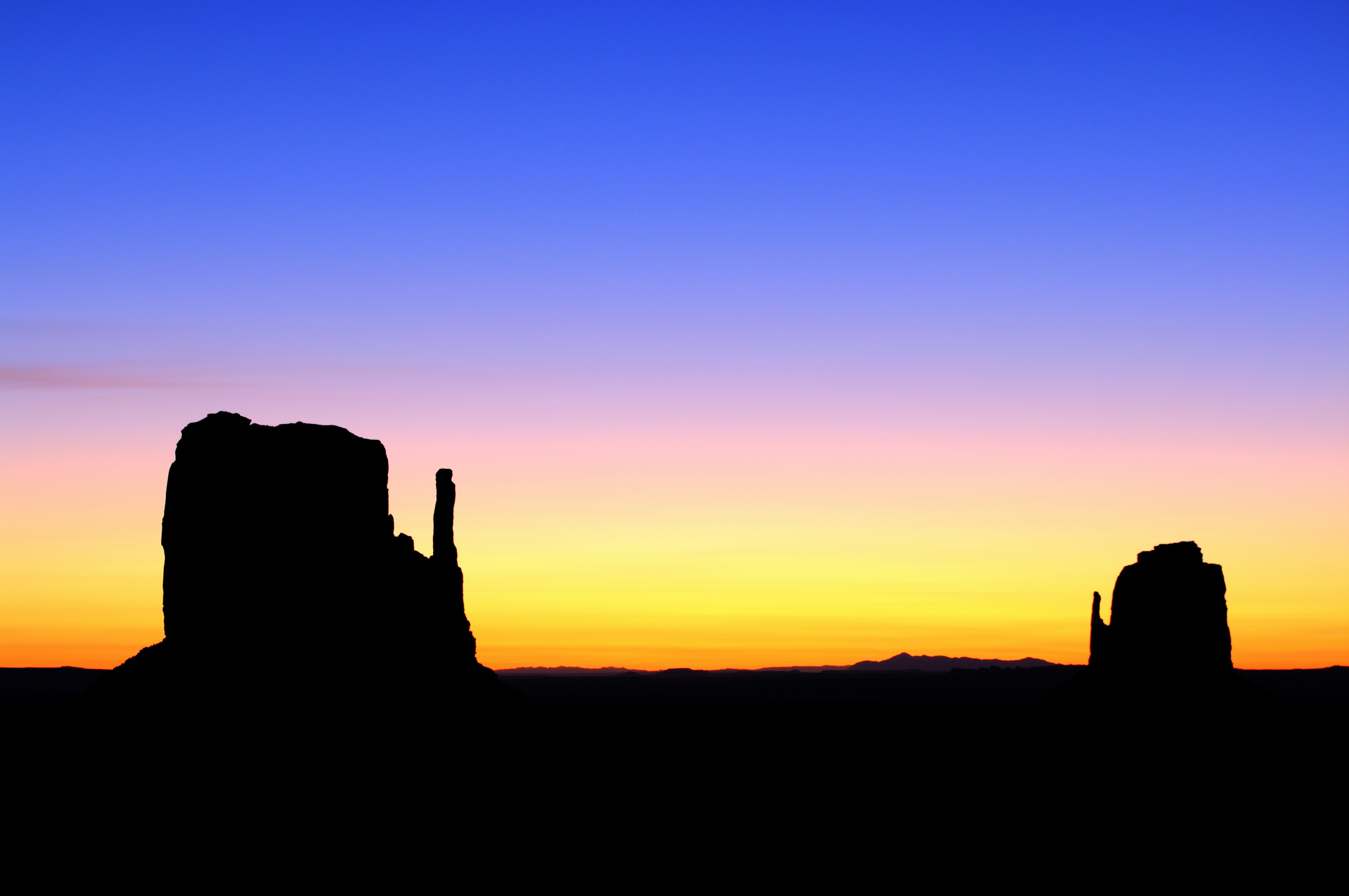 Silhueta do nascer do sol das Mittens em Monument Valley perto de Oljato, Estados Unidos, contra um céu vívido em laranja e azul.