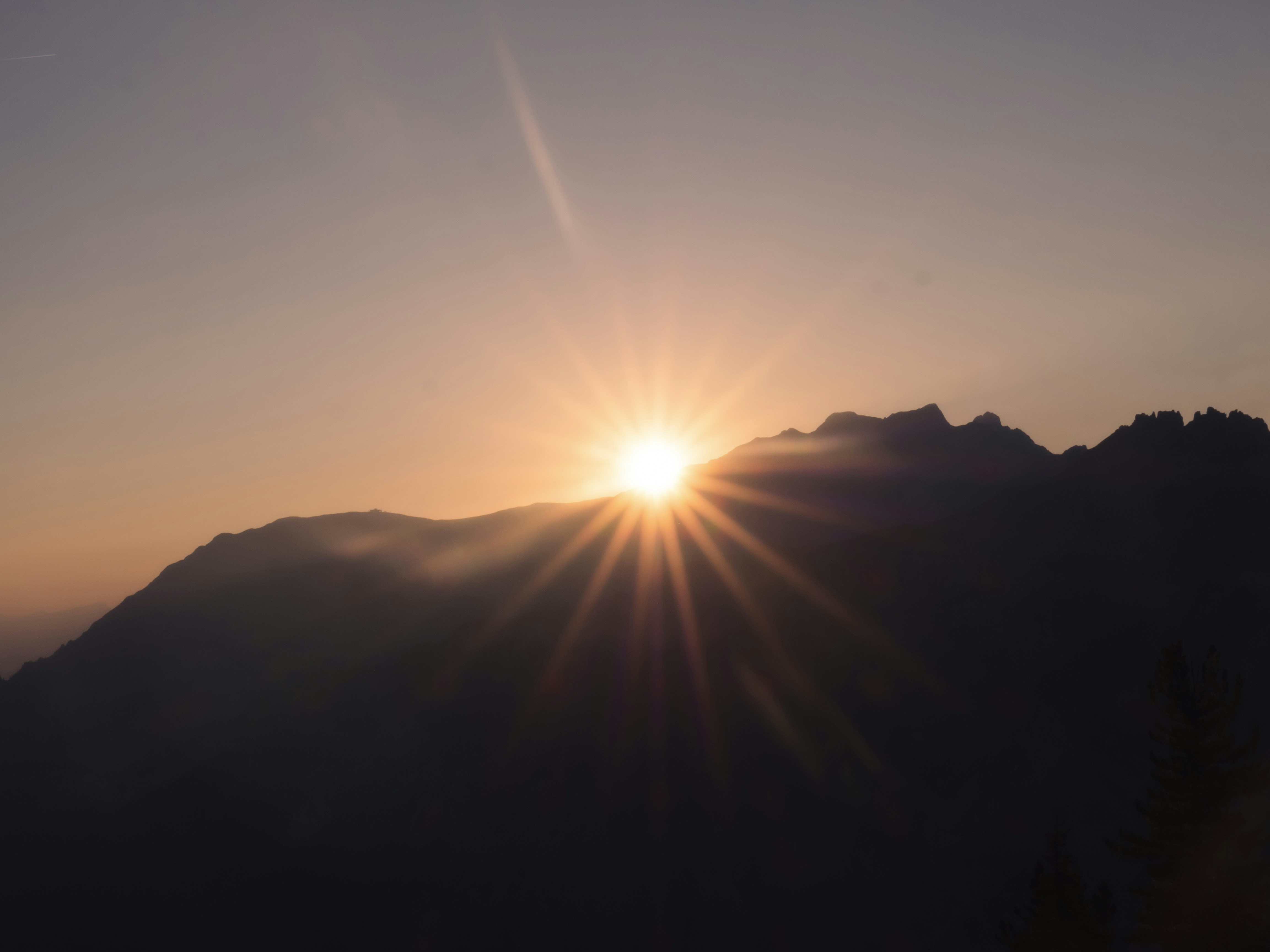 Peisaj montan cu soare răsărind, raze de lumină peste munți verzi, cerul portocaliu și roz în zori
