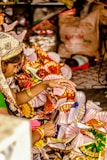 A person is engaged in a colorful craft activity, surrounded by vibrant paper fans or decorations. The hands are actively working with the materials, suggesting careful craftsmanship. The background contains various items, adding a sense of a busy, possibly festive environment.
