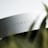 A close-up of a sleek, white object with the word 'CORSAIR' printed on its surface. The focus on the brand name suggests it is a piece of technology or an accessory. There is a blurred foreground element that appears to be a green plant, adding a natural contrast to the modern object.