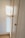 A wooden wardrobe with simple round knobs on the doors, bathed in soft natural light creating warm tones. The light casts a square shadow on the adjacent white wall, suggesting a nearby window.