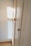 A wooden wardrobe with simple round knobs on the doors, bathed in soft natural light creating warm tones. The light casts a square shadow on the adjacent white wall, suggesting a nearby window.