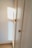 A wooden wardrobe with simple round knobs on the doors, bathed in soft natural light creating warm tones. The light casts a square shadow on the adjacent white wall, suggesting a nearby window.