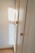 A wooden wardrobe with simple round knobs on the doors, bathed in soft natural light creating warm tones. The light casts a square shadow on the adjacent white wall, suggesting a nearby window.