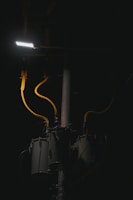 A dimly lit scene features a streetlight illuminating part of a utility pole with several cylindrical transformers. The cables are prominently highlighted in yellow against the dark background.