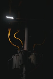 A dimly lit scene features a streetlight illuminating part of a utility pole with several cylindrical transformers. The cables are prominently highlighted in yellow against the dark background.