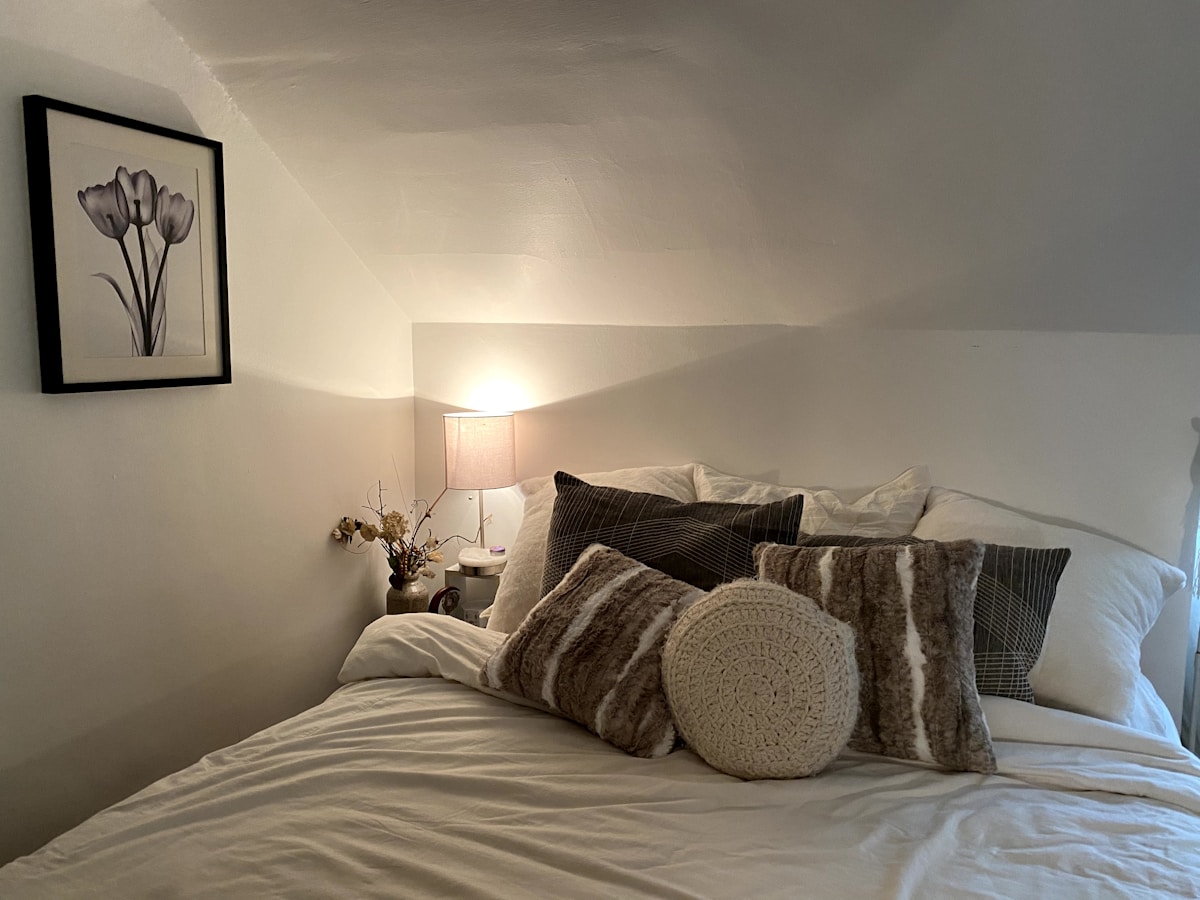 cozy small apartment bedroom with warm lamp light and layered throw pillows
