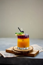 A vibrant cocktail being poured into a glass with fresh herbs and fruits.