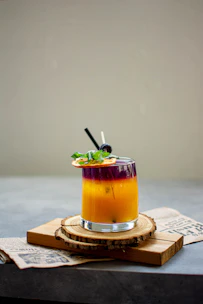 A vibrant cocktail being poured into a glass with fresh fruit garnishes on a wooden bar.