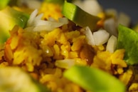 A close-up of a dish featuring vibrant yellow rice mixed with sliced avocados, chopped white onions, and visible beans.