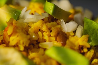 A close-up of a dish featuring vibrant yellow rice mixed with sliced avocados, chopped white onions, and visible beans.