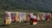 A colorful display of traditional clothing hanging on racks is set against a lush green hillside. Garments in various vibrant colors such as red, yellow, blue, and pink are shown. A small stall with a red cloth on top offers various items, possibly headwear or accessories.