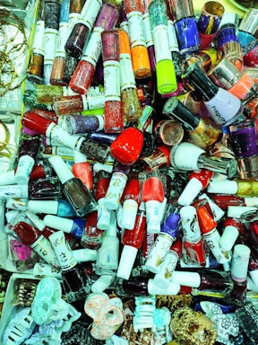 A vibrant collection of nail polish bottles showcased in various colors, including reds, blues, pinks, purples, and glitters, alongside some hair accessories. The assortment is dense, creating an eye-catching display of cosmetics.