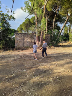 Couple walking hand in hand along a rustic path framed by terracotta walls and soft sand.