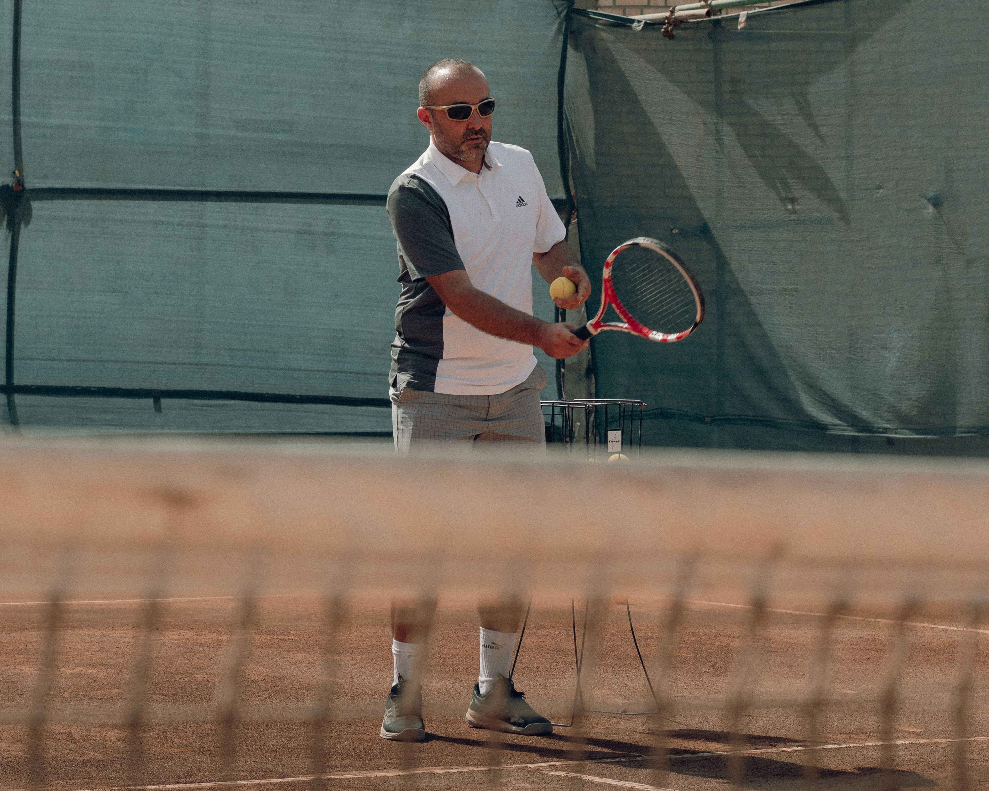 The tennis coach is feeding the ball to his student.