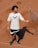 A person stands on a clay tennis court, wearing a white t-shirt with a logo and black shorts. A tennis racquet is being tossed or caught in the air, casting a shadow on the ground.