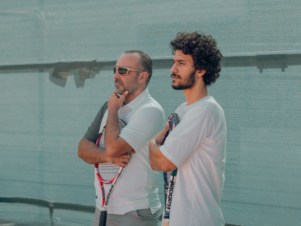 a couple of men stand near each other holding tennis rackets