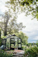 A sleek glass greenhouse bathed in morning sunlight with lush plants inside.