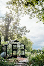 A bright outdoor glass sitting room surrounded by lush greenery.