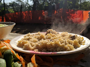 A vibrant rice bowl topped with fresh ingredients, beautifully plated on a rustic wooden table at a sunny outdoor event.