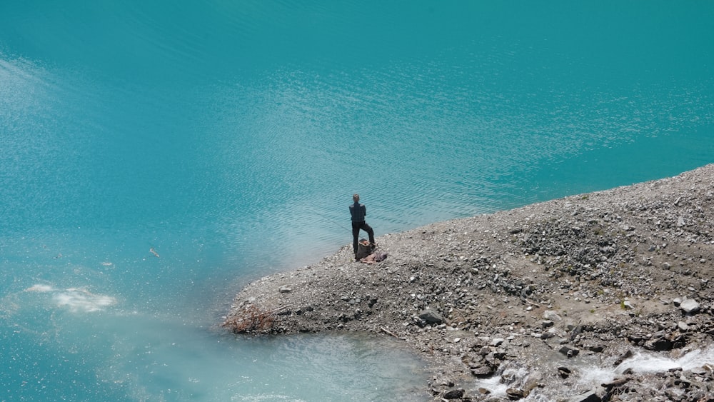 a man and woman standing on a rocky shore by the water