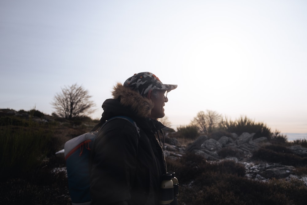 a man wearing a hat and a backpack standing on a rocky hill