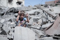 A girl making the victory sign over the rubble of a destroyed home in Gaza.