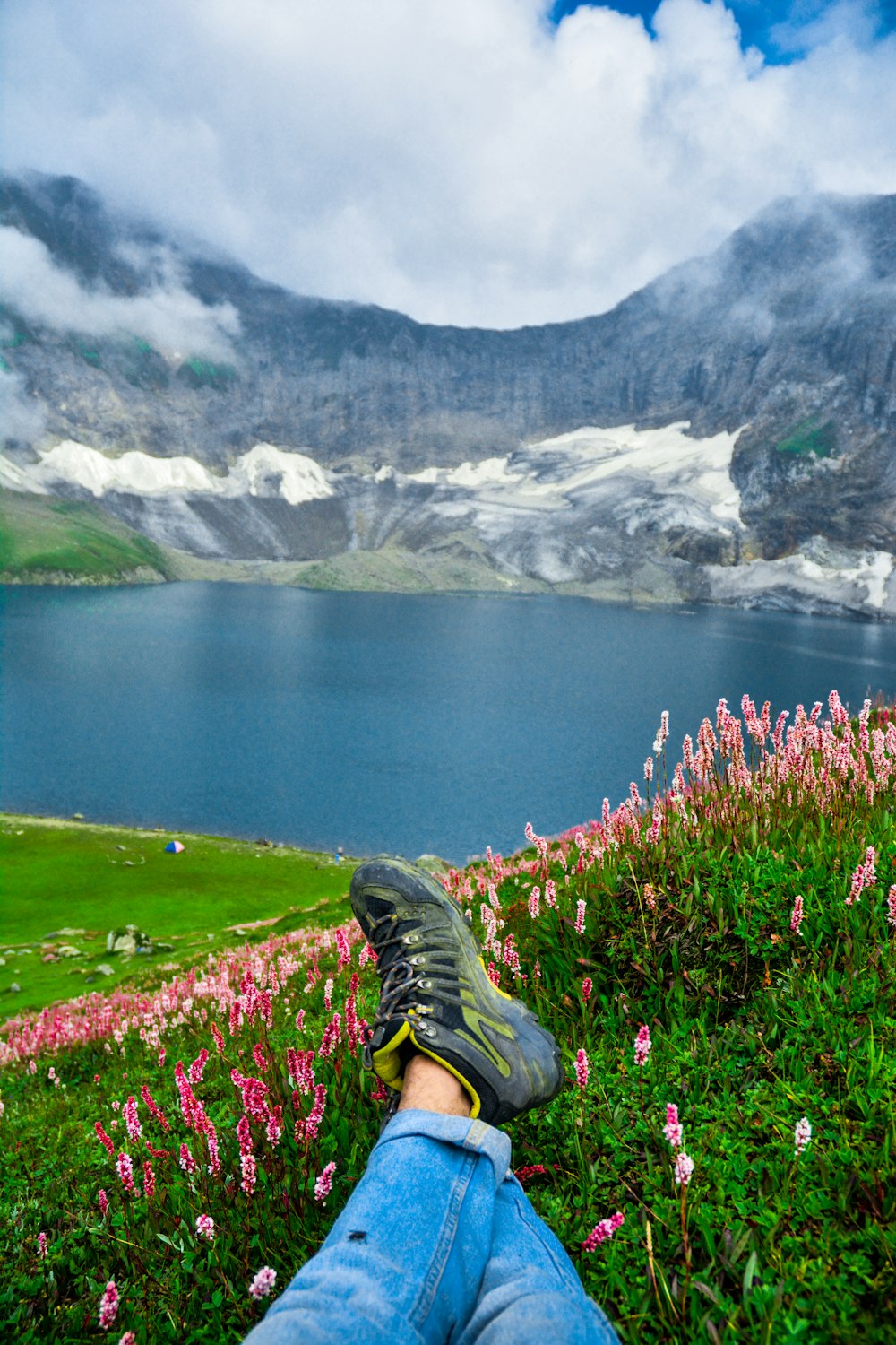 a person's feet on a grassy hill overlooking a lake