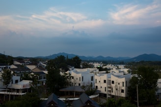A serene landscape showing a harmonious blend of modern eco-friendly buildings nestled among lush green trees under a bright blue sky.