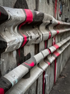 A textured concrete surface features wavy horizontal bars painted with red, black, and white graffiti. The setting appears to be an urban environment, possibly part of a street or graffiti artwork. The visual style is edgy and abstract.