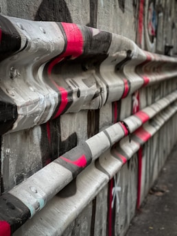 A textured concrete surface features wavy horizontal bars painted with red, black, and white graffiti. The setting appears to be an urban environment, possibly part of a street or graffiti artwork. The visual style is edgy and abstract.