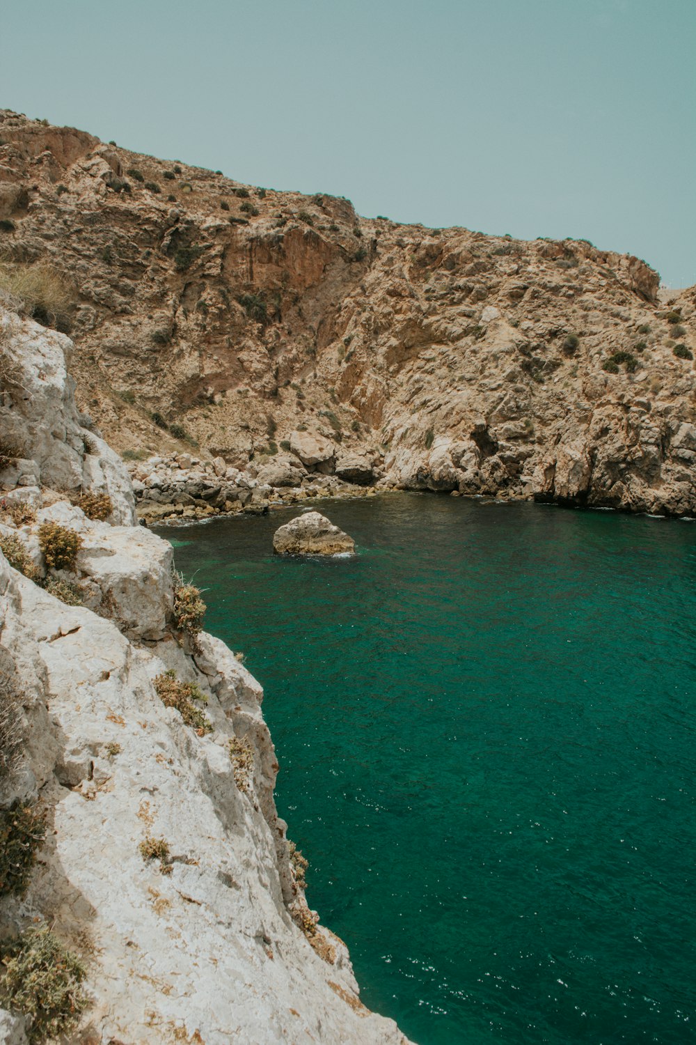 a body of water with a rocky cliff and a blue sky