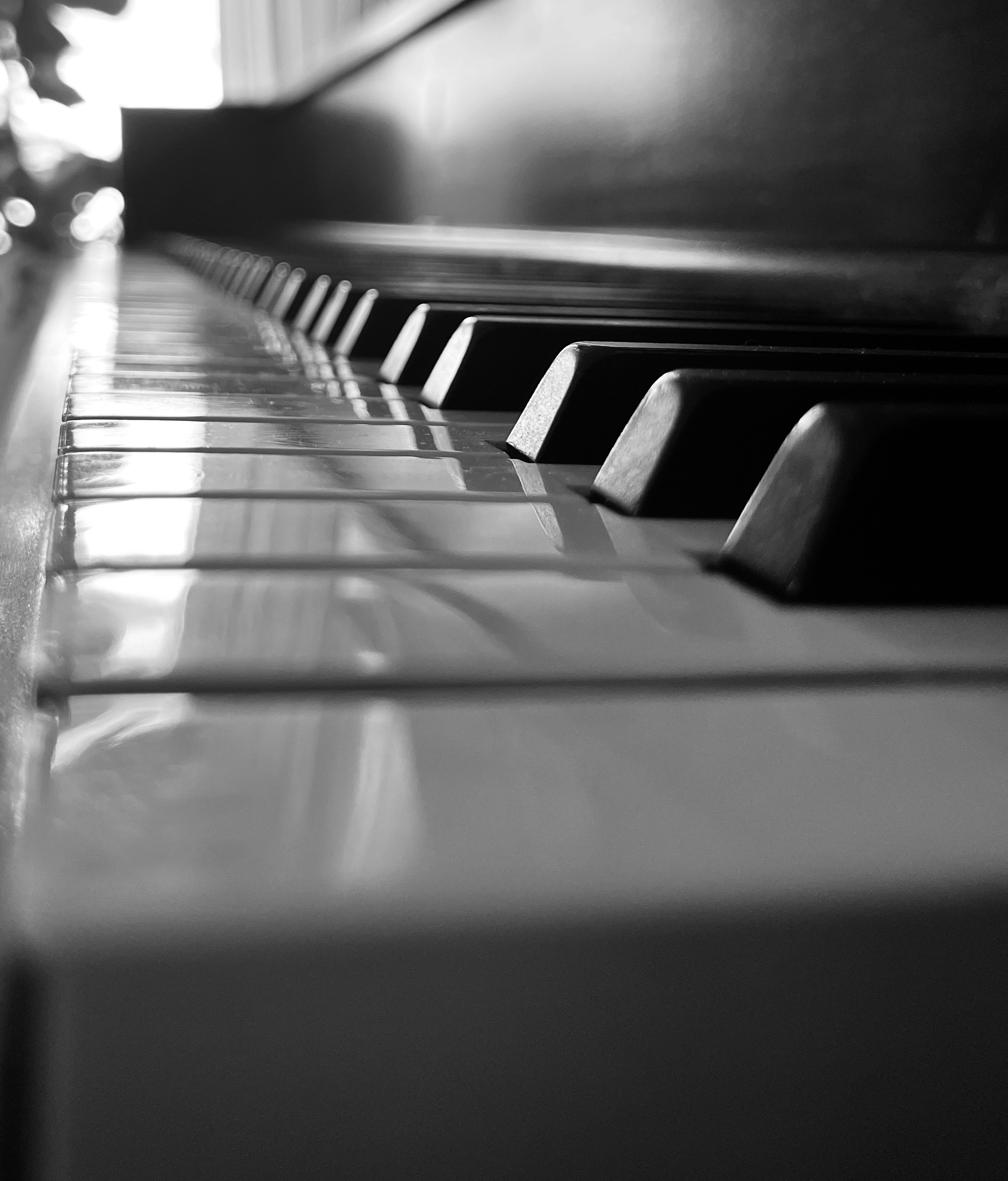 Grand piano keys close-up, dramatic side lighting, dark atmospheric studio, deep shadows, ivory keys