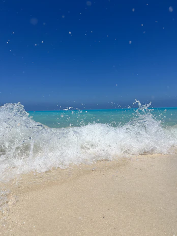 Turquoise waves gently washing onto a pristine sandy beach under a bright sky