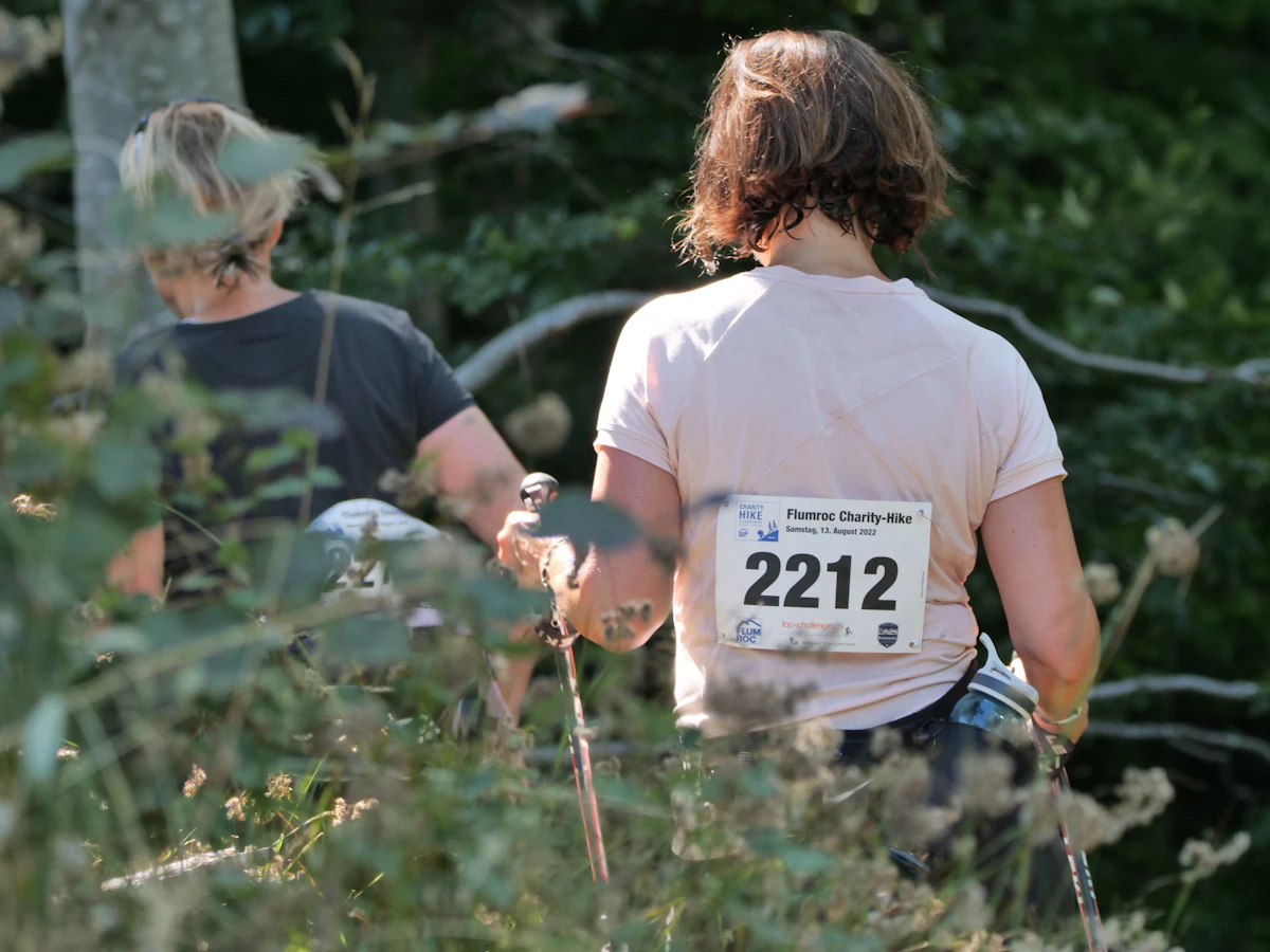 Two walkers wearing race bibs on a wooded charity course, seen from behind