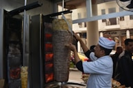 Chef preparing döner meat on the vertical rotisserie with flames in the background.