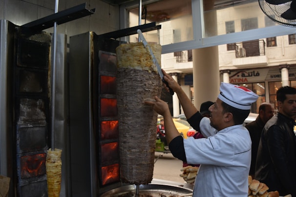 Grilled donair meat being sliced in a busy kitchen setting.