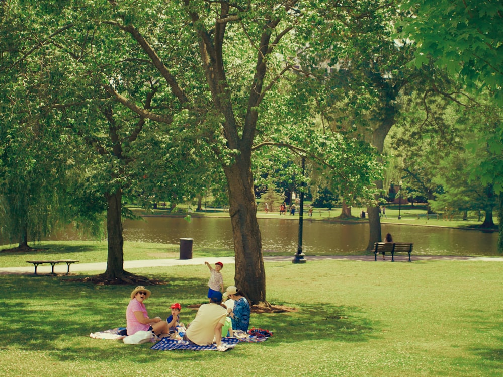 a group of people sitting on the grass by a lake