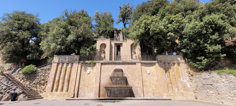 a stone wall with a building on it and trees in the back