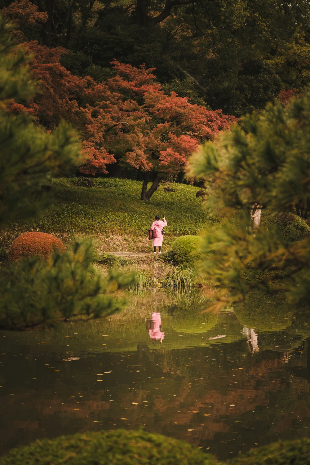 a couple of people walking on a path by a pond with trees