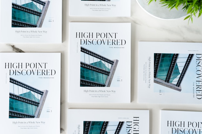 Multiple copies of 'High Point Discovered' magazines arranged on a light surface, featuring a modern architectural building on the cover.